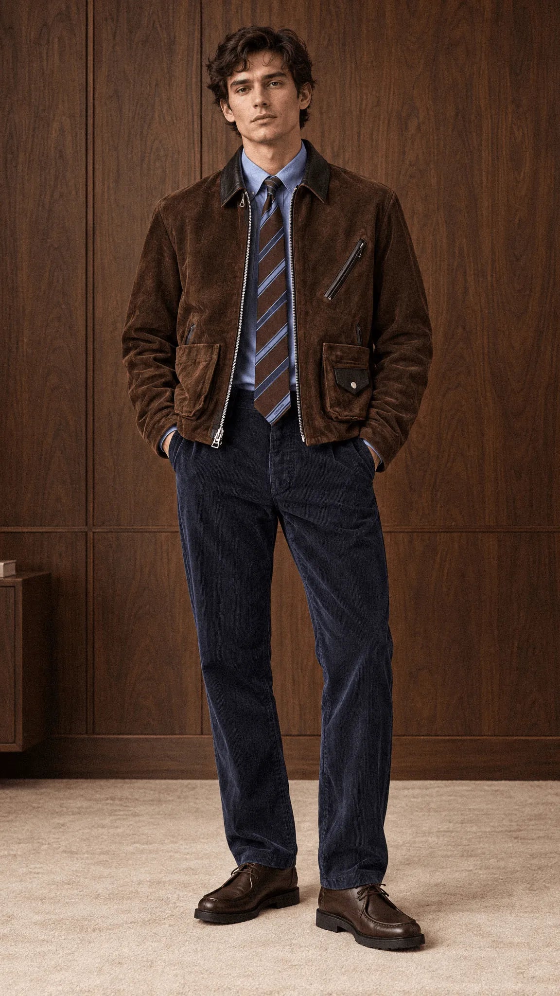 A male model wears a Sacai brown suede jacket patch with leather collar details and match with ralph laurent corduroy blue pants and bottega venetta mocassino shoes, with Ferragamo brown and blue stripes tie.