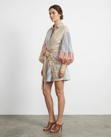 Woman wearing a multicolored striped dress with a belt against a white background