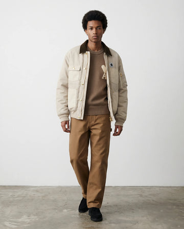 Man wearing a Carhartt beige jacket and brown pants standing against a white background